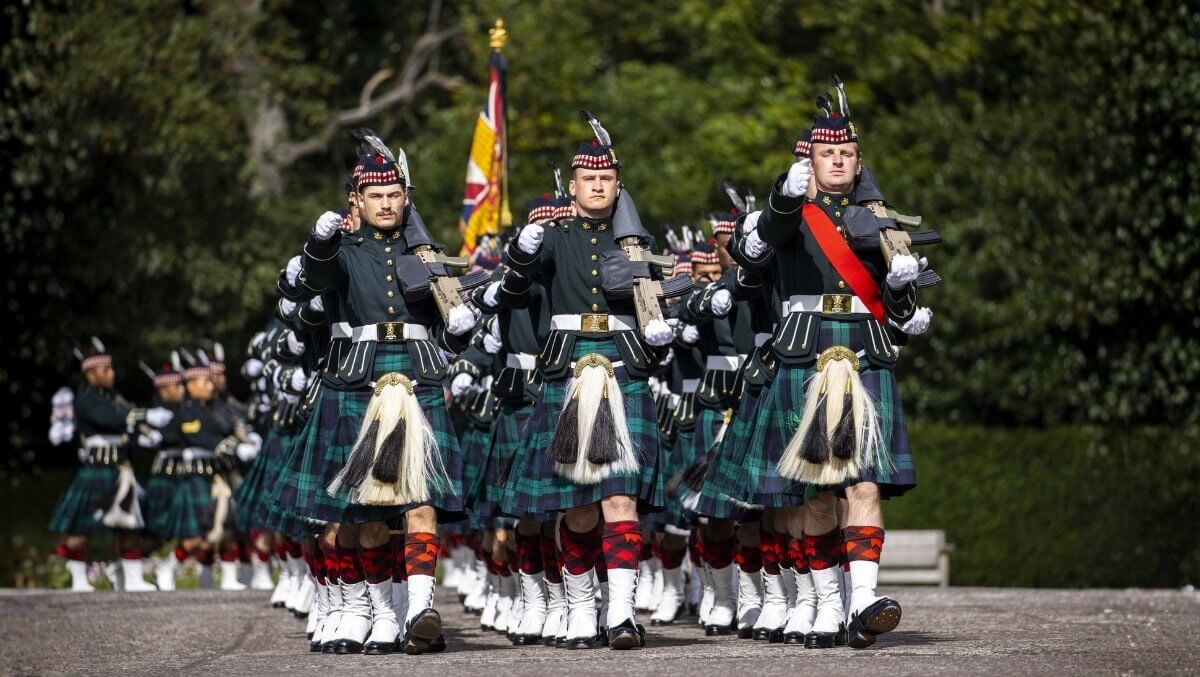 Black Watch soldiers in tartan kilts marching in formation during a ceremonial parade honoring Scottish military tradition.