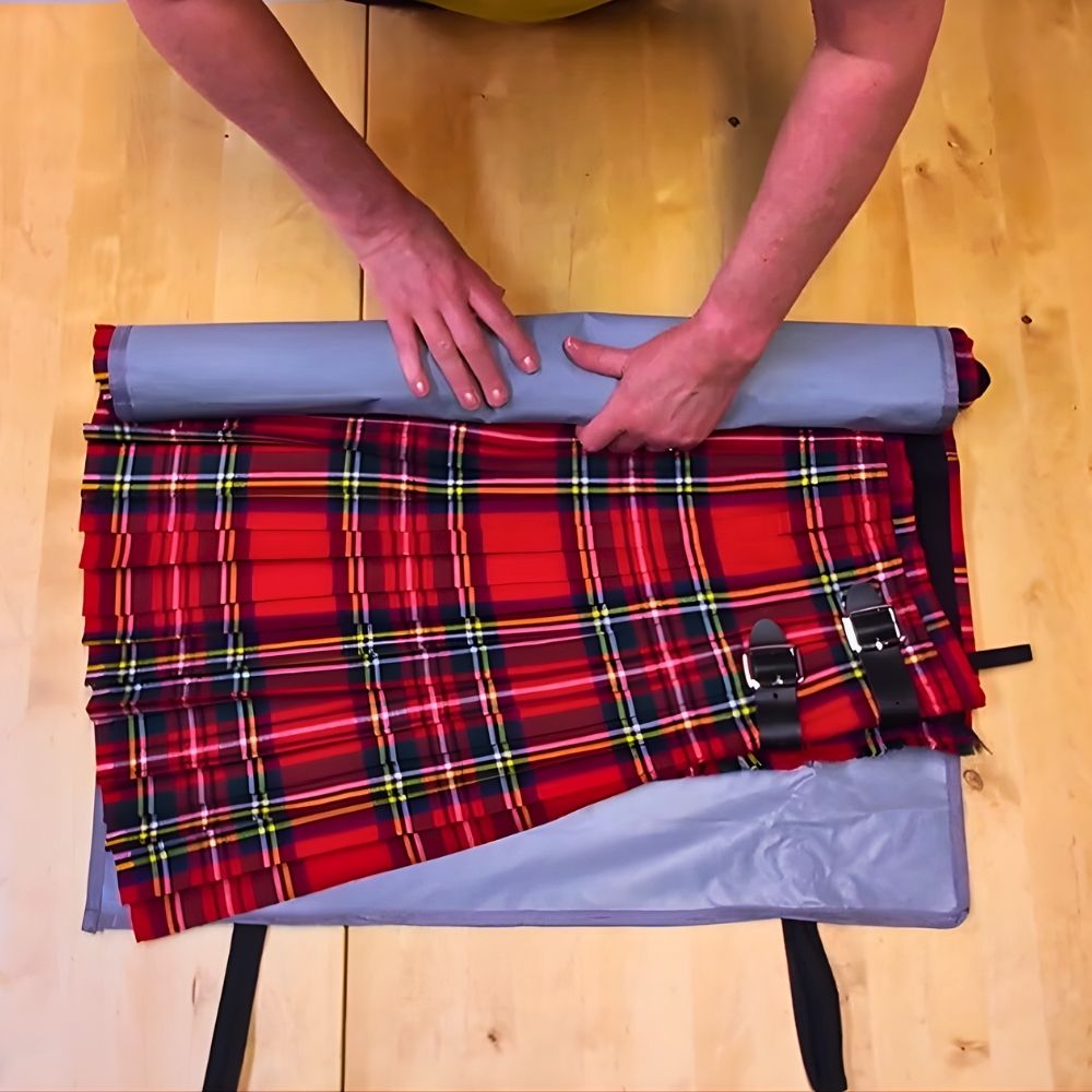Person rolling a red tartan kilt on a cloth wrap to protect the pleats for travel.