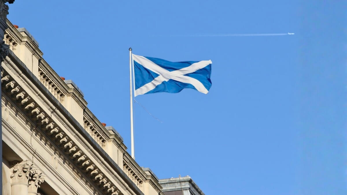 Scottish Saltire flag waving atop a building against a clear blue sky with architectural details in view.