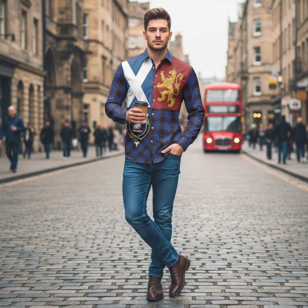 Man sitting indoors wearing a navy sweater with a white diagonal Saltire-style cross on the chest.