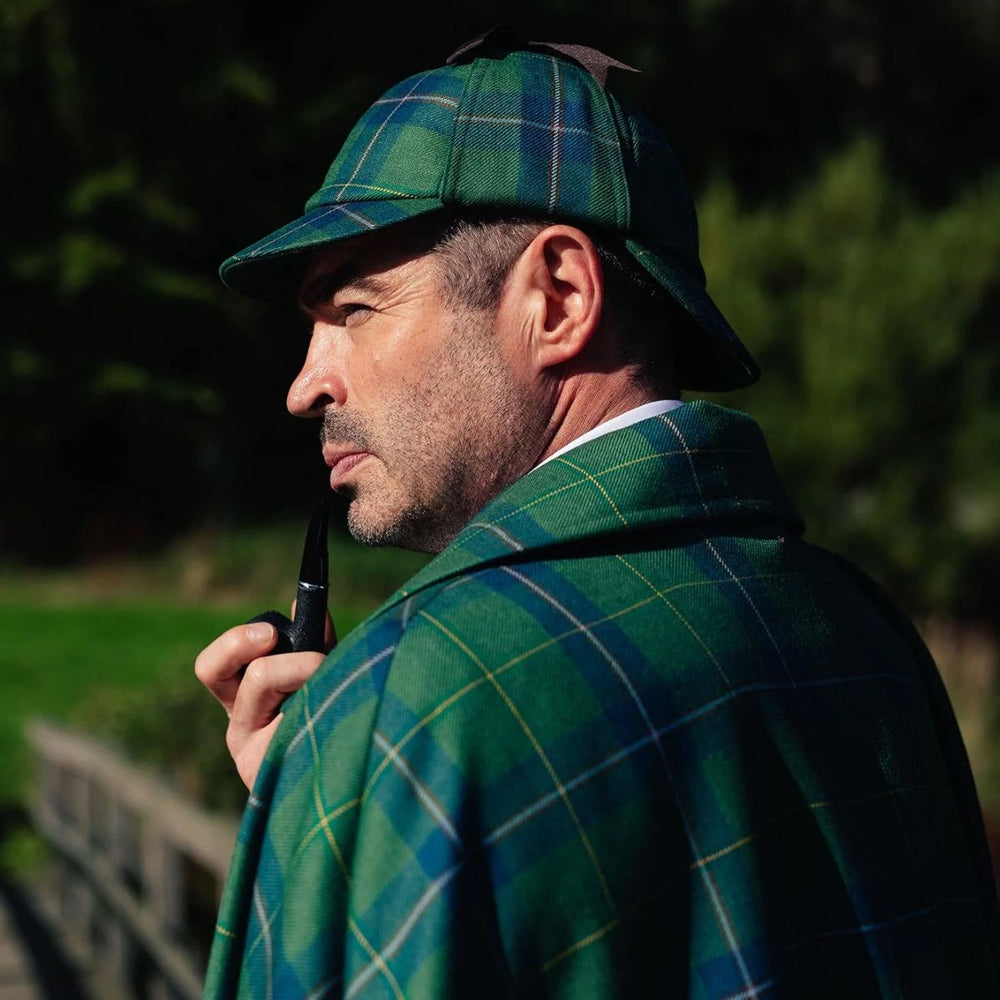 Man wearing a green tartan deerstalker hat and cloak while holding a pipe.