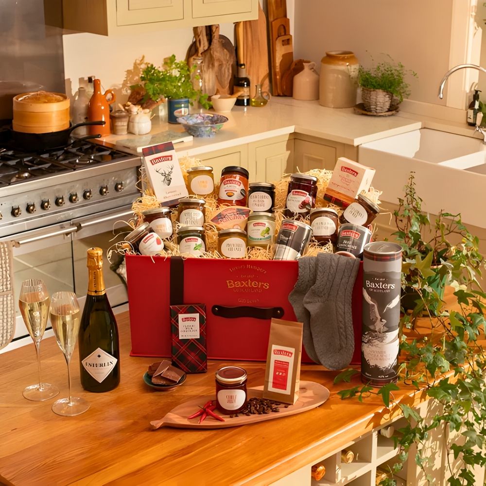 A festive gift basket featuring assorted Scottish products, including preserves, biscuits, coffee, wine, and specialty items in a warm kitchen setting.