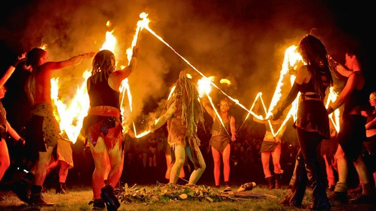 Modern Samhain ritual with participants in dark costumes dancing around fire and symbolic offerings in a night ceremony.