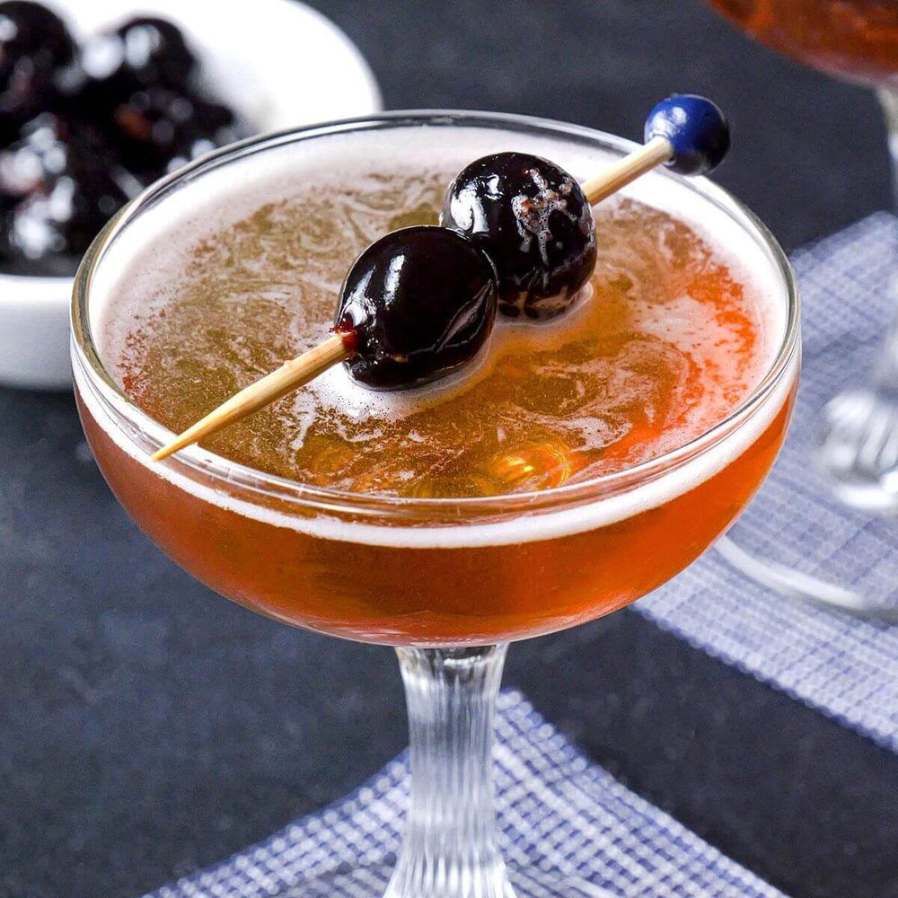 Rob Roy cocktail garnished with cherries in a coupe glass