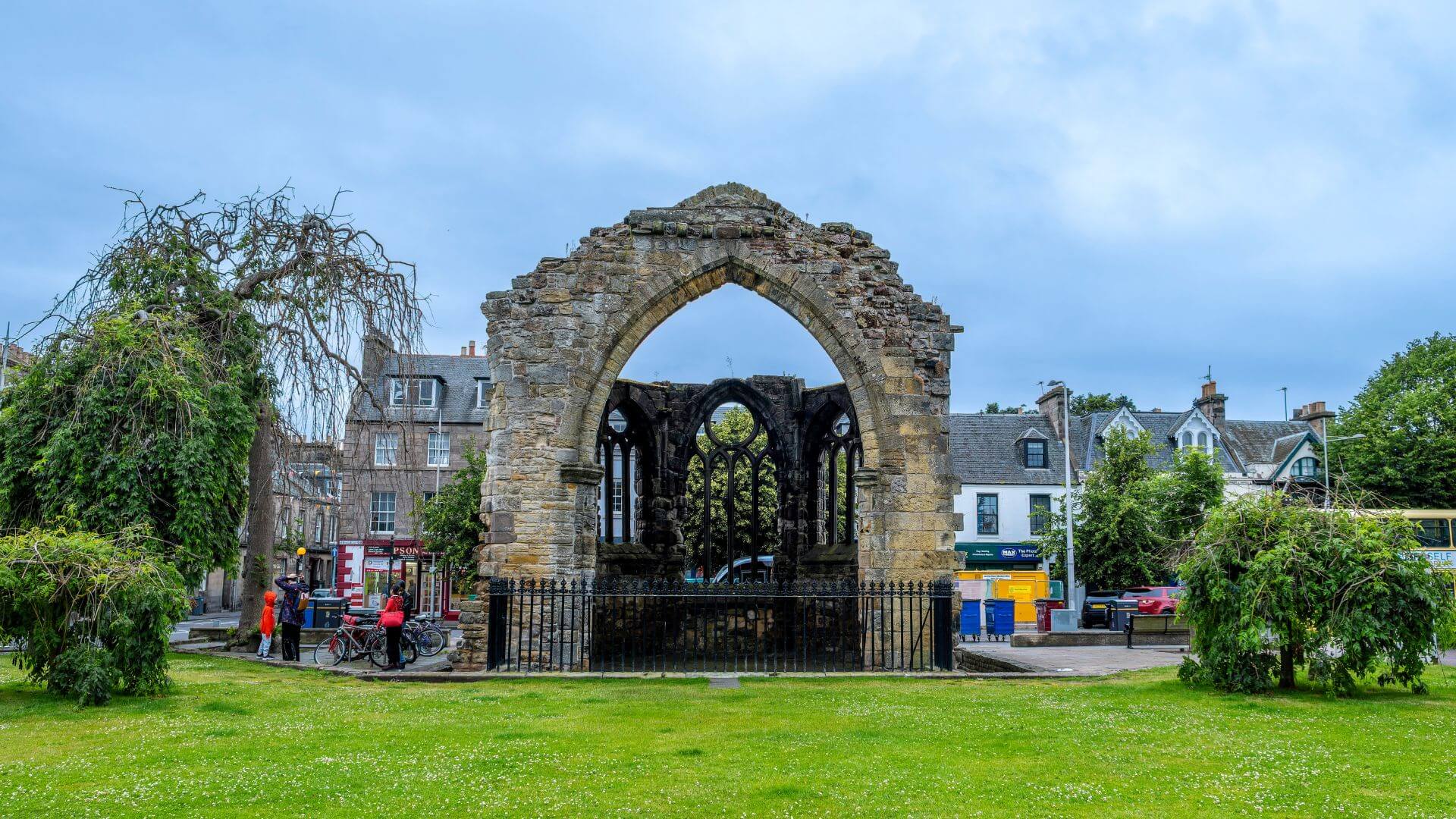 Ruins of Blackfriars Chapel in St Andrews, Scotland — featuring a historic stone arch and Gothic windows set against a backdrop of traditional town buildings and greenery.
