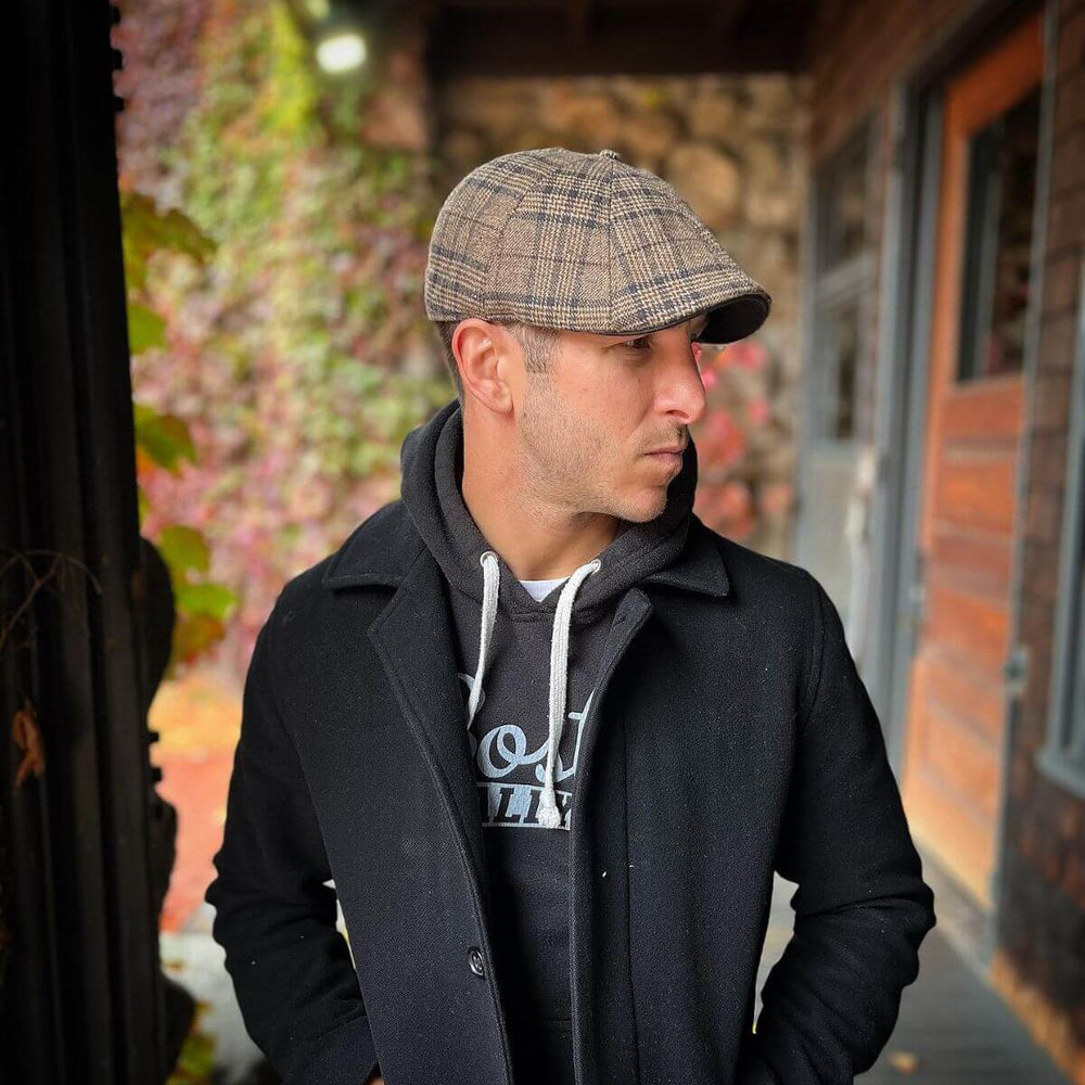 Man wearing a brown plaid scally cap paired with a black coat outdoors