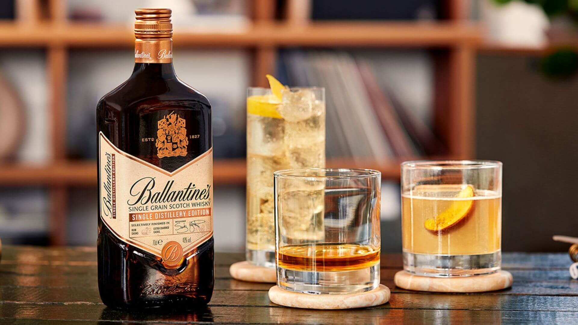 Ballantine’s single grain Scotch whisky bottle with whisky cocktails and glasses on wooden table