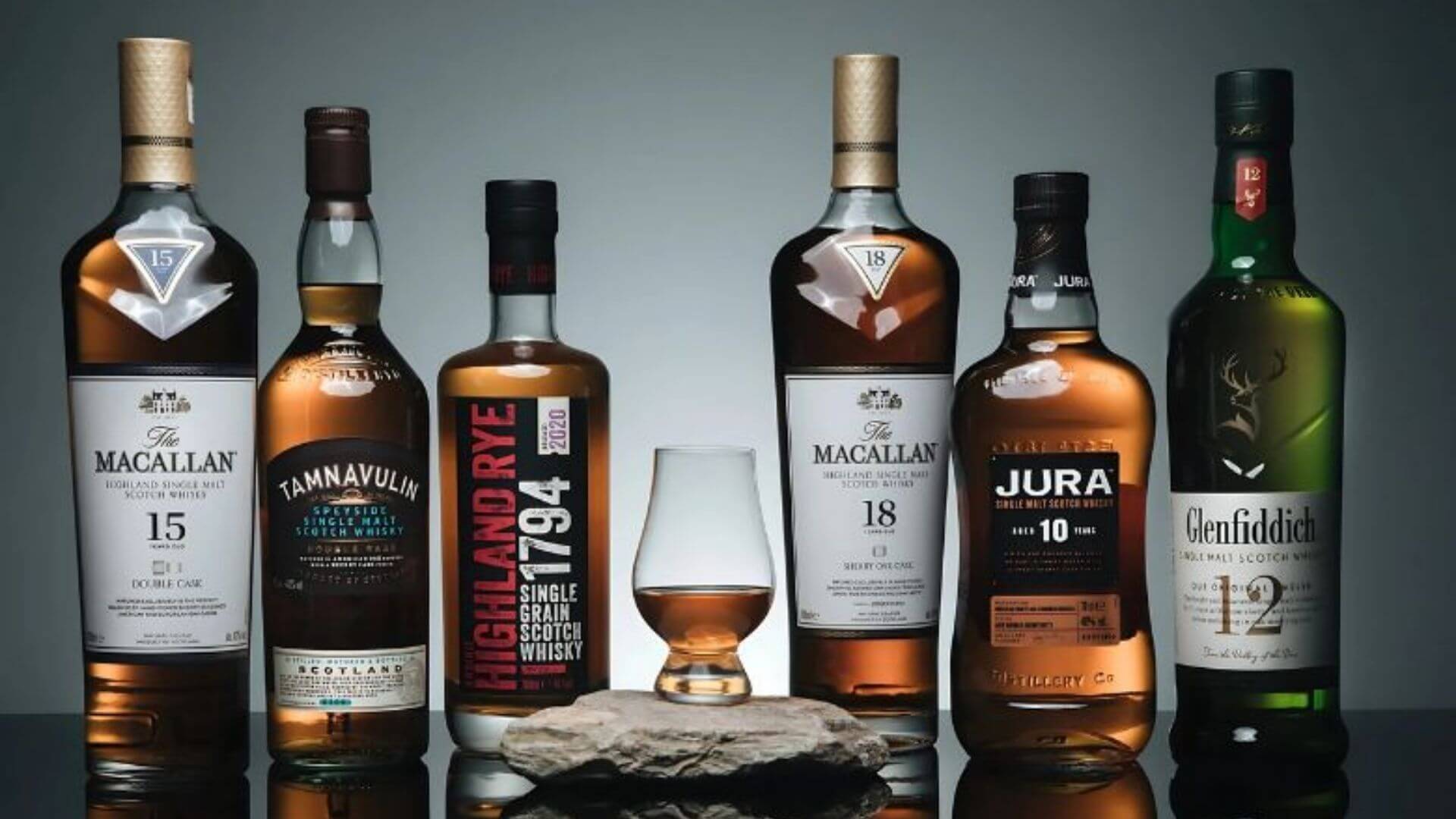 Premium single malt Scotch whisky bottles including Macallan, Jura, Glenfiddich, and Tamnavulin displayed with tasting glass