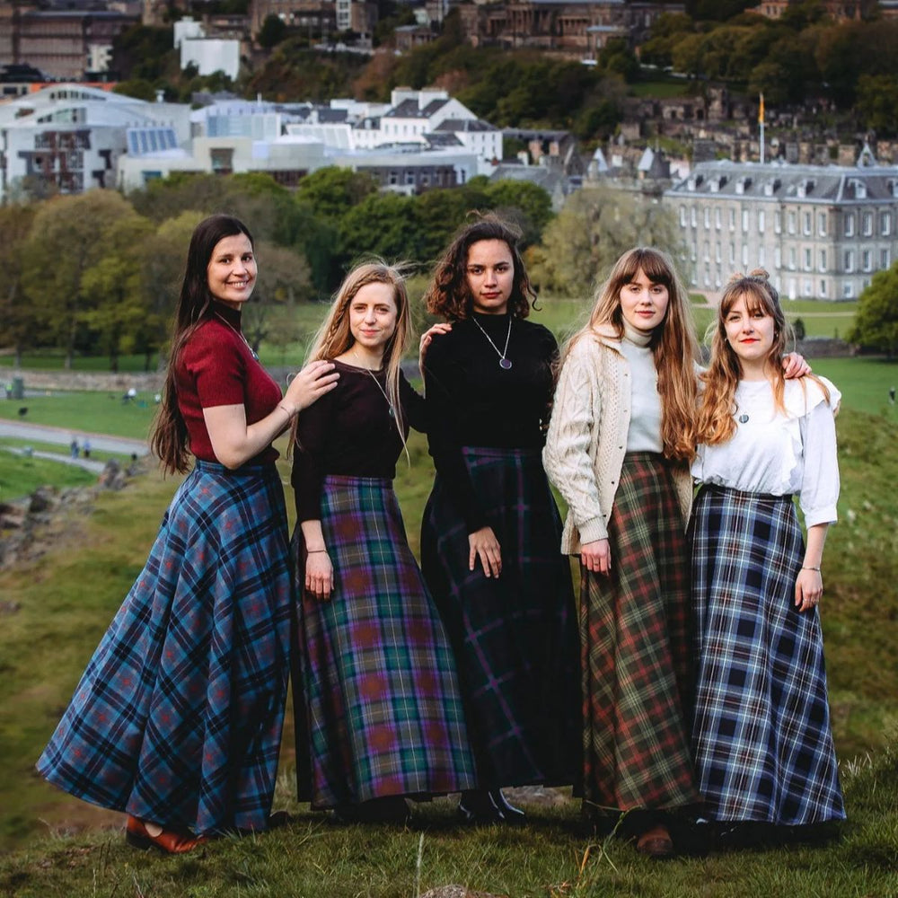 Group of women wearing tartan maxi skirts in traditional Scottish plaid, posing outdoors in Edinburgh