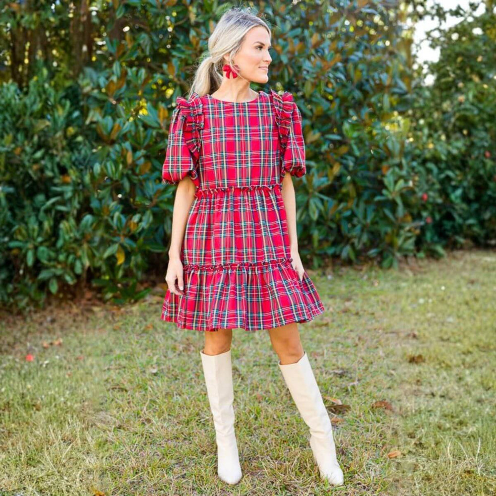 Woman wearing a red tartan ruffle dress with puff sleeves and knee-high boots outdoors