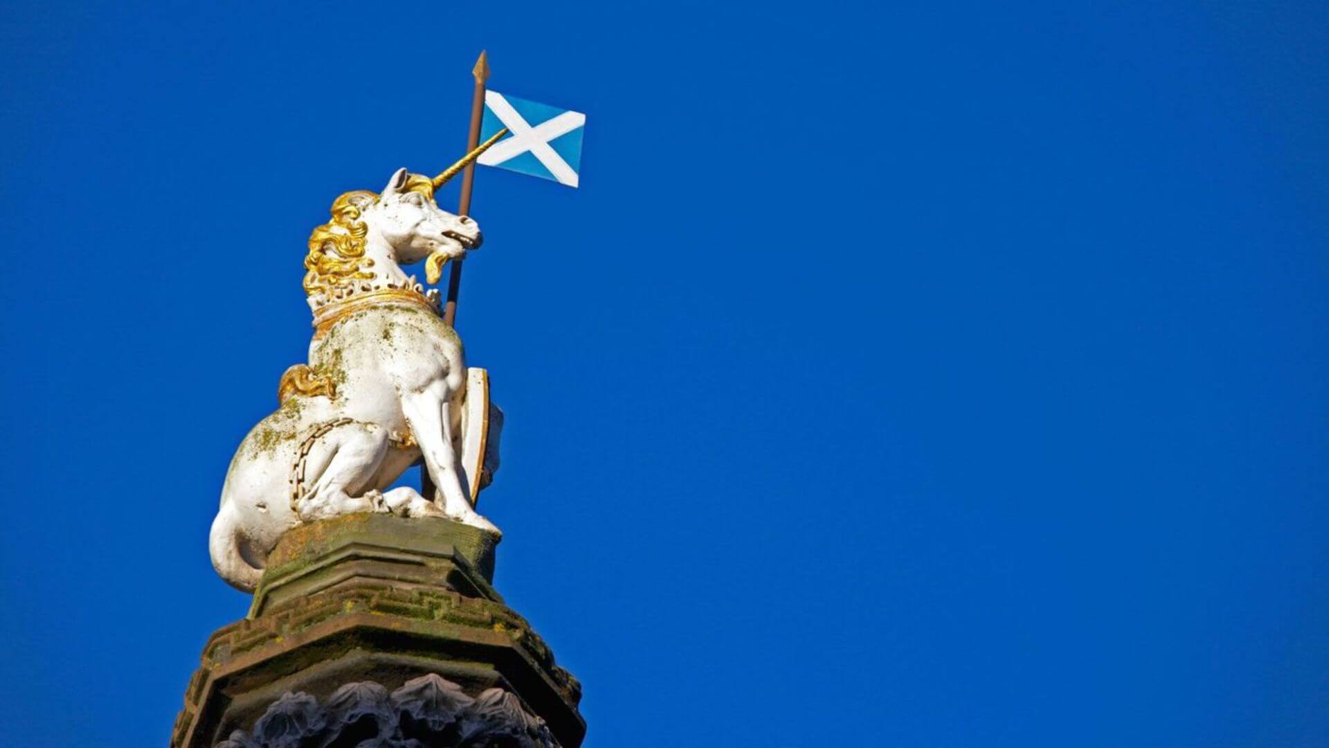 Unicorn statue holding the Scottish flag against a clear blue sky.