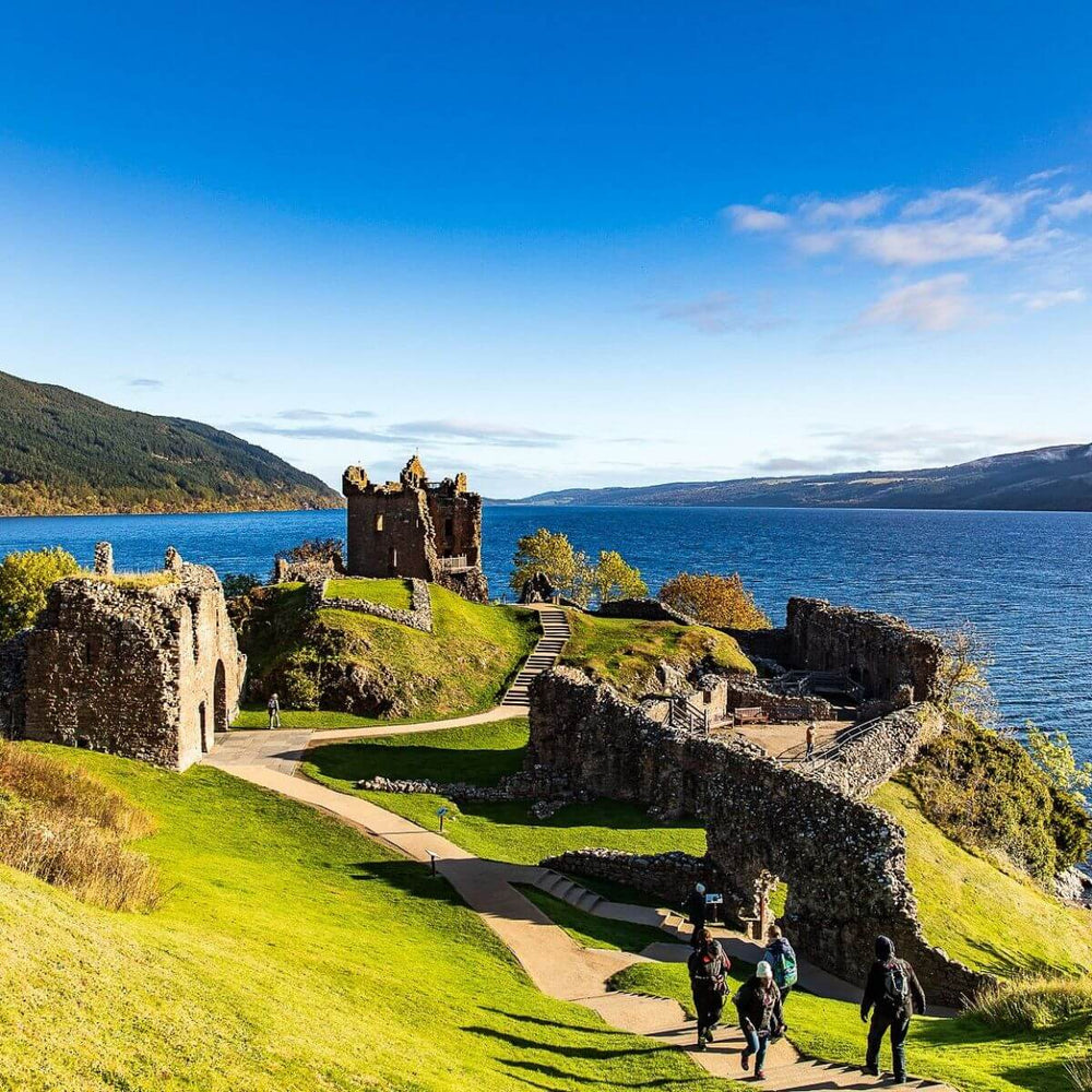 Ruins of Urquhart Castle overlooking Loch Ness in the Scottish Highlands under a bright blue sky.