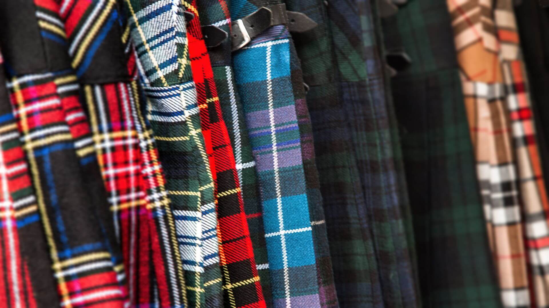 Scottish tartan fabrics in various clan patterns displayed in colorful kilt designs